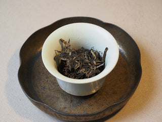 Premium dry loose raw puerh tea leaves placed neatly inside a ceramic gaiwan brewing vessel.
