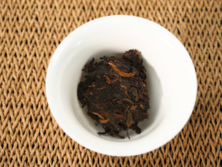 Dry 2020 Bojun Ripe Pu-erh leaves loaded in a white porcelain gaiwan before brewing, on a woven jute mat.