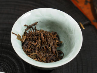 Close-up of the infused wet tea leaves of 2021 Dayi Guanchao Raw Puerh Tea in a celadon bowl, showing healthy, plump leaf quality.
