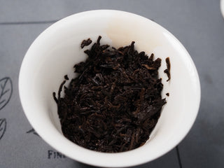 Wet, dark brown brewed tea leaves (cha di) of Dayi 7572 ripe puerh inside a white gaiwan.
