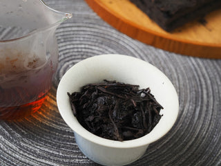 Wet, opened-up ancient tree tea leaves of the 2013 Lincang Ripe Pu-erh resting inside a white ceramic gaiwan after brewing.