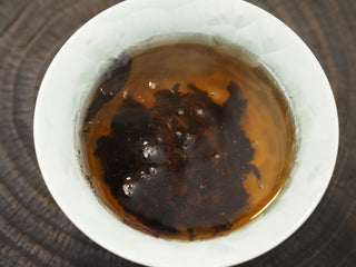 Bright, deep reddish-brown brewed tea liquor of Dayi 7592 ripe puerh inside a green celadon cup.