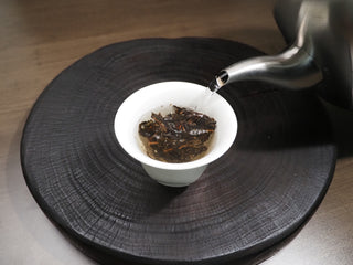 Pouring hot water from a kettle into a white gaiwan containing 2021 Dayi Mi Xiang Raw Puerh tea leaves.

