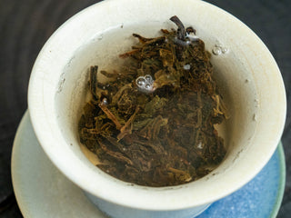 Rinsing and awakening the 2006 aged raw Puerh tea leaves with hot water in a porcelain Gaiwan.