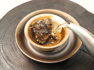Boiling water being poured into a ceramic gaiwan over Gold Brick 2012 sun-dried White Peony tea piece, beginning the infusion.