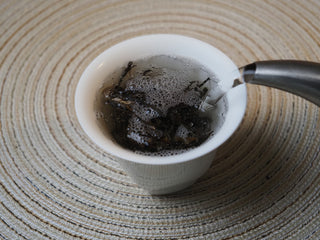Hot water being poured over 2026 Tan Chun raw Puerh tea leaves during brewing.