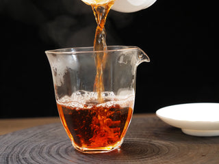 Pouring bright amber-red ripe puerh tea from a Gaiwan into a glass fairness cup (Cha Hai).