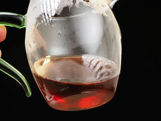 Rich burgundy-red tea liquor of brewed Dayi 7572 ripe puerh held in a glass fairness cup.