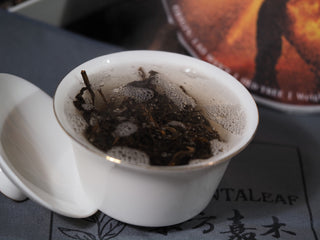 Delicate early spring ancient tree Lao Man'e Puerh tea leaves steeping inside a white porcelain Gaiwan.