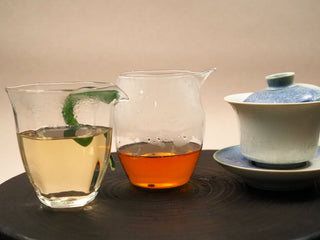 Comparison of first and second steeps of 2014 Fuding Shou Mei waffle cake: plain pitcher and green-handle pitcher beside a gaiwan.