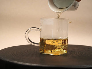 Golden amber tea liquor from 2014 Fuding White Peony waffle cake poured from a gaiwan into a glass fairness pitcher.