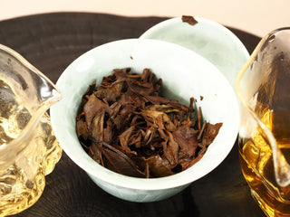 Dark wet steeped leaves of 2018 Fuding Shou Mei in a gaiwan flanked by two glass pitchers of amber tea liquor.