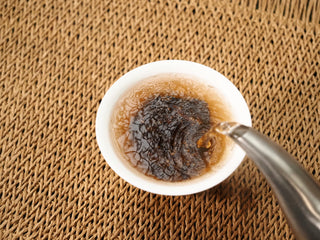 Boiling water poured from a metal kettle into the gaiwan of 2020 Bojun leaves, the liquor turning deep reddish brown.