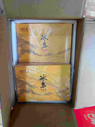 Open cardboard shipping carton containing two sealed golden boxes of Mengku Rongshi Bingdao Aged Ripe Pu-erh (320g each).