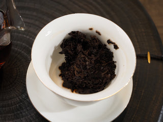 Wet, plump, and dark reddish-brown fermented tea leaves of Dayi 7572 ripe puerh in a Gaiwan after steeping.