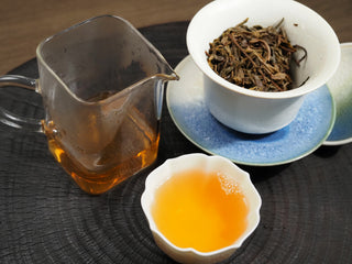 A Chinese gongfu tea set displaying the brewed Dayi 7542 puerh tea soup, glass pitcher, and gaiwan.