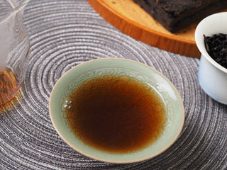 A small tea cup filled with the rich, clear reddish-brown liquor of the 2013 Dry-Aged Lincang Ripe Pu-erh tea.