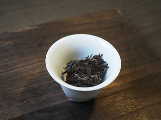 Dry Mangfei Mountain raw Pu-erh tea leaves in a white porcelain tasting cup