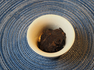 Dry aged Shou Pu-erh tea leaves resting inside a white ceramic tasting gaiwan