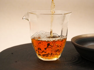 Deep red-brown tea liquor from Gold Brick 2012 aged White Peony poured from a gaiwan into a glass fairness pitcher.