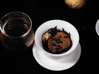 Wet, infused Xinhui citrus peel and dark ripe Pu-erh tea leaves inside a white gaiwan after steeping.