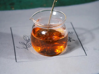 Pouring brewed Jingyang Golden Flower Fu Brick Tea into a glass Gongdao cup, showing clear, reddish-brown tea liquor.