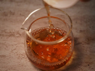 Tea liquor from 2019 Lincang Ancient Arbor Sheng Pu-erh Tea Cake being poured into a glass fairness pitcher showing clear bright color