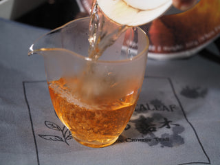 Pouring the clear and golden Lao Man'e raw Puerh tea liquor from a Gaiwan into a fairness cup.