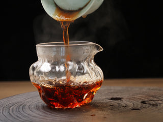 Streaming dark red ripe puerh tea from a brewing vessel into a hammered glass fairness pitcher (Cha Hai).
