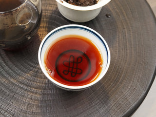 A ceramic cup filled with thick, bright reddish-brown Dayi 7572 ripe puerh tea liquor, viewed from above.