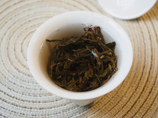 Infused wet leaves of 2026 Tan Chun raw Puerh tea resting in a white tasting cup.