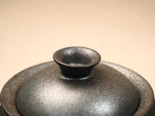 Close-up of the knob on a wood-fired stoneware gaiwan lid from Dehua Fujian, smooth glazed finial against rough textured lid.