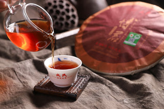2019 Bojun Ripe Pu-erh poured from a glass pitcher into a small branded cup, the liquor a clear deep reddish amber.
