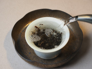 Hot water being poured over dry raw puerh leaves in a gaiwan during the initial tea rinse.