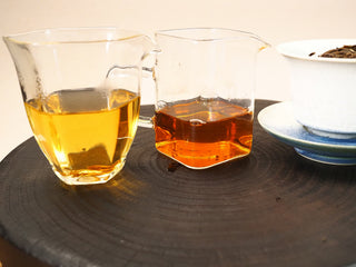 Two glass pitchers of 2020 Fuding White Peony showing the color shift from gold to reddish amber, with a gaiwan beside.