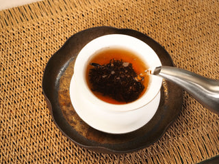 Boiling water poured from a metal kettle into the gaiwan of Bojun Ripe Pu-erh 7.0 leaves, the liquor turning deep reddish brown.