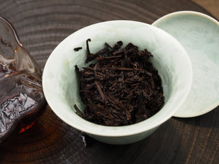 Steeped wet tea leaves and stems of Dayi 7592 ripe puerh in a green celadon bowl, showing the fermented leaf bottoms.