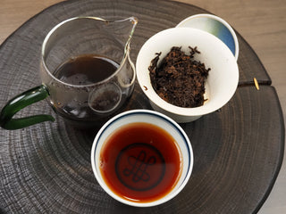 Complete Gongfu tea session setup for 2019 Dayi 7572 ripe puerh, showcasing a Gaiwan with wet leaves, a glass pitcher, and a cup of red tea liquor.