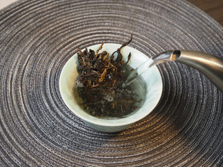 Hot water being poured over 2025 Tan Chun raw Puerh tea leaves during brewing.