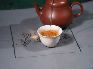 Brewed Jingyang Golden Flower Fu Brick Tea poured into a small Chinese tea cup, showcasing the rich aroma and clear reddish-brown liquor.