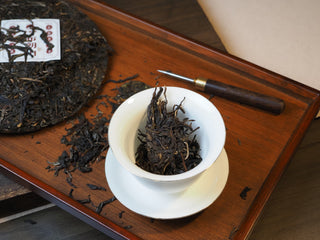 Loose raw pu-erh tea leaves measured in a white ceramic gaiwan for brewing