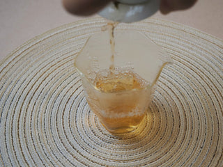 Pouring brewed 2026 Tan Chun raw Puerh tea liquor from a gaiwan into a fairness pitcher.