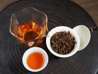 Complete tea session setup featuring 2016 Dayi 7532 raw Puerh tea soup in a cup, pitcher, and wet leaves in a Gaiwan.