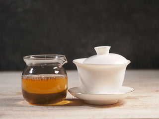 Side view of gaiwan and gongdao cup side by side, displaying the vivid amber tea liquor of 2019 Qilin Tribute Sheng Pu-erh Tea Cake – Ancient Arbor 357g.