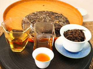 Full gongfu brewing scene of 2020 Fuding White Peony with cake, two pitchers of liquor, a tasting cup, and leaves in a gaiwan.