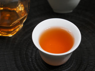 A cup of freshly brewed 2021 Dayi Mi Xiang Raw Puerh tea, showcasing its bright, clean orange-gold tea liquor.
