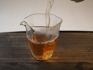 Clear golden-yellow tea liquor of Mangfei Mountain raw Pu-erh in a glass fairness pitcher