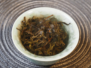 Infused wet leaves of 2025 Tan Chun raw Puerh tea resting in a white tasting cup.