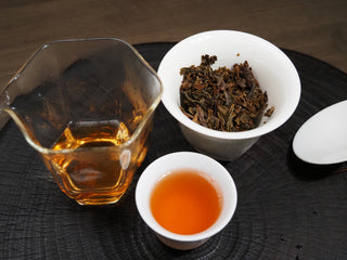 Chinese Gongfu tea tasting set with brewed 2021 Dayi Mi Xiang Raw Puerh tea, glass gongdao bei, and wet leaves in a gaiwan.
