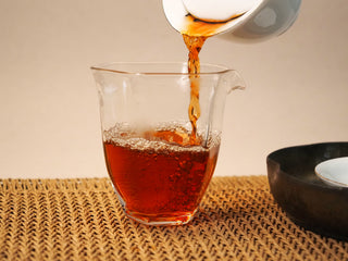 Bojun Ripe Pu-erh 7.0 tea poured from a gaiwan into a glass pitcher, the liquor streaming in a clear deep reddish amber color.